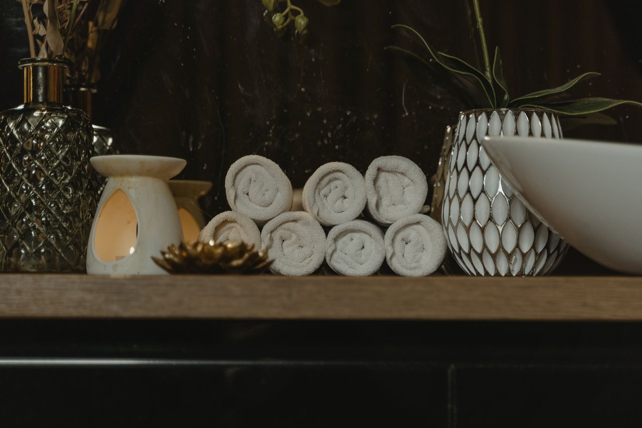 Rolled white towels beside a candle and decorative vases on a wooden spa shelf.